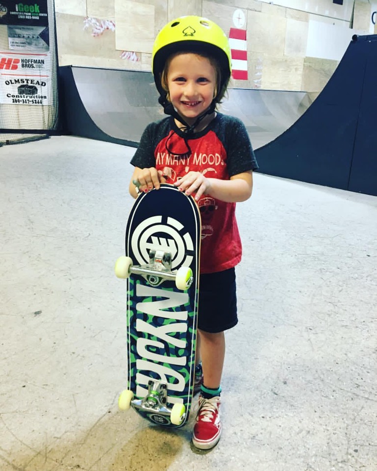 A young rider in a red hoodie holding a skateboard up in front of them