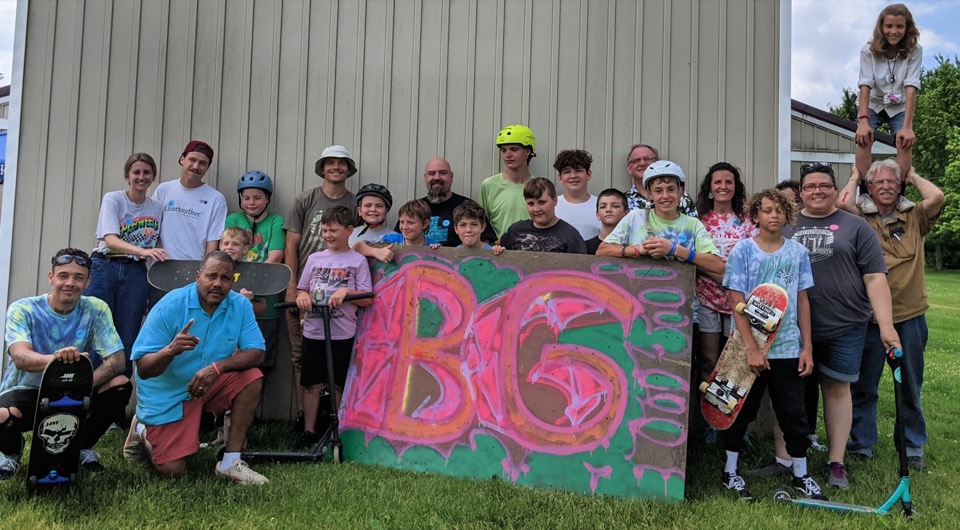 A large group of kids and adults outside a Battleground summer camp session, holding a hand-painted BG sign