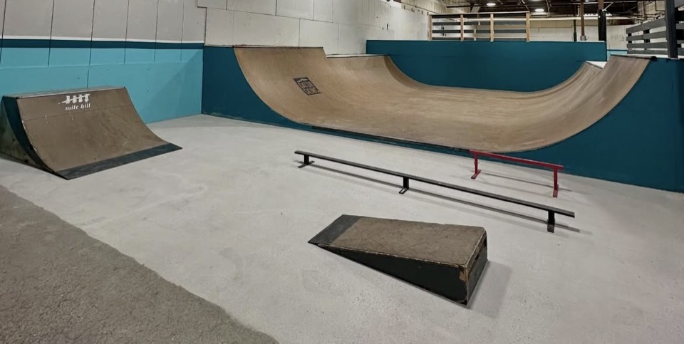 The concrete bowl and ramps inside Battleground, with the teal park walls behind them